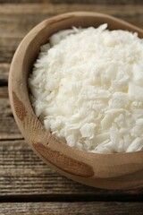 White soy wax flakes in bowl on wooden table, closeup