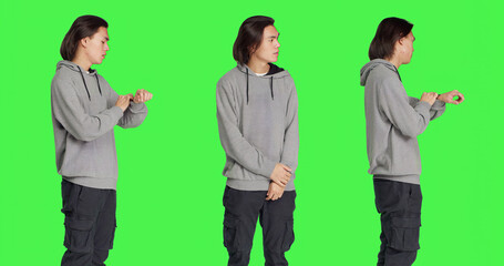 Young male model looks at watch standing against greenscreen backdrop, acting impatient in studio....