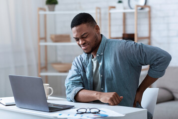 Pain In Back. African American Guy Having Backache Massaging Aching Lower Back Suffering From Pain Sitting At Workplace In Modern Office. Lumbar Ache. Health Problem Concept.