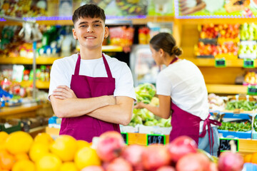 Portrait of positive young salesman in the vegetable section of a grocery store