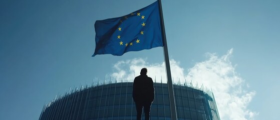 silhouette of a person standing in front of a large flag against a clear sky