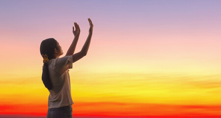 Fototapeta premium Cute girl worshipping God on sunset colorful sky background.