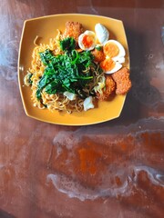 A plate of instant noodles topped with spinach, hard-boiled eggs, and fried fish cakes.