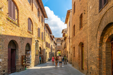 Fototapeta premium Tourists walk the narrow pedestrian streets near the Porta San Giovanni main gate in the Tuscan hilltop village of San Gimignano, Italy.