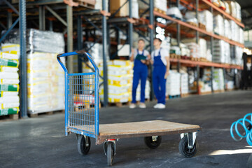 Empty cargo cart stands against background of warehouse with workers