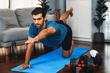 Flexible and dexterity man in sportswear doing yoga position in meditation posture on exercising mat at home. Healthy gaiety home yoga lifestyle with peaceful mind and serenity.