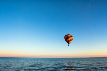 Obraz premium Colorful hot air balloon flying over a calm sea with a clear blue sky.