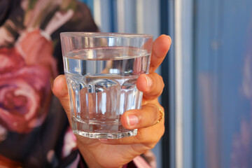 A Hand Holding a Clear Glass of Fresh Water Set in a Beautiful and Colorful Atmosphere
