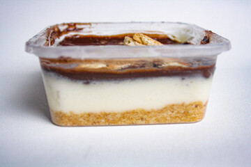 Sweet dessert in a plastic container with chocolate, whipped cream, and biscuit on white background