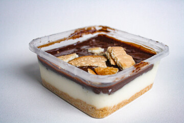 Sweet dessert in a plastic container with chocolate, whipped cream, and biscuit on white background