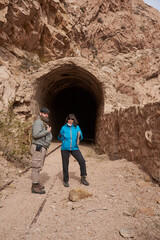 Couple of friends, man and woman, walking on the train tracks in a mountainous area of Potrerillos, Mendoza, Argentina. Behind them there is a tunnel.