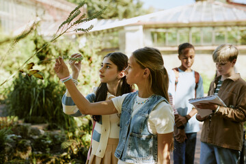 Group of teen girls and boys studying plants growing in local botanical garden on sunny day