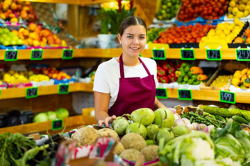 Young saleswoman working and posing in store near counter with fresh round bottlegourd vegetable