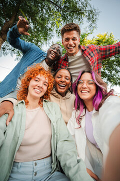 Group of happy teenagers smiling and having fun outdoors, enjoying friendship and diversity while taking a selfie together in a park on a bright sunny day. Young friends smiling and laughing