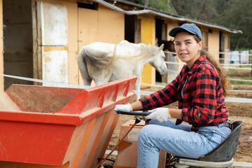 Young girl works on tractor - transporting hay for horses in a stable