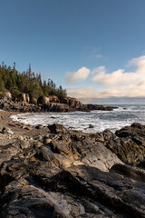 rocky beach in the north east maine waves crashing on rocks pine trees by the coast clouds in the blue sky