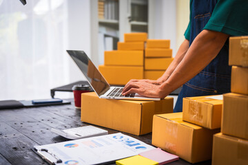 Close-up of a businessman’s hand packing items at a desk, preparing products for shipping....
