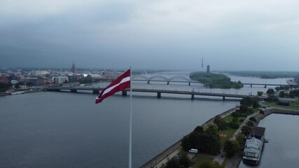 Moody and stormy day over Riga city with waving Latvia flag, aerial orbit view