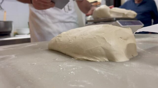 Closeup view of the hands of a white pastry chef cutting and weighing whe dough for his homemade pastries in his traditional bakery. Spain.