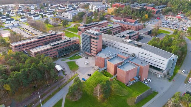 Aerial view of a modern university campus in Kristiansand, Norway. Red brick buildings, green spaces, and a bustling student life create a vibrant atmosphere for learning and research. Reverse 4k
