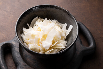 Dried coconut chips in a bowl on a dark background vertical photo