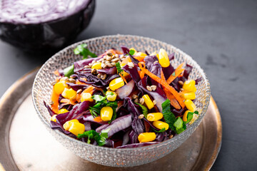  Fresh salad with red cabbage, carrots, hemp seeds and corn in a bowl on the table close up