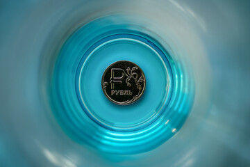 Russian Rubles at the bottom of the blue glass. the concept of the ruble's fall.