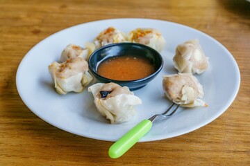 A close-up photo of a plate of dim sum, showcasing the delicate folds of wrappers and the steaming hot filling