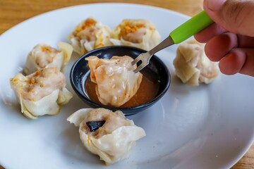 A close-up photo of a plate of dim sum, showcasing the delicate folds of wrappers and the steaming...
