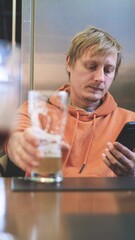 Close-up of man using smartphone while drinking beer in pub.