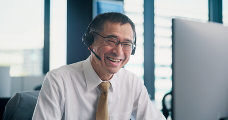 Office, businessman and computer with mic for call center, telemarketing and support for customer service. Japanese, happy person and mature agent with headset for listening, research and sales goals