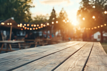 Empty wooden table providing space for product placement at an outdoor summer festival with string lights and blurred people in the background at sunset