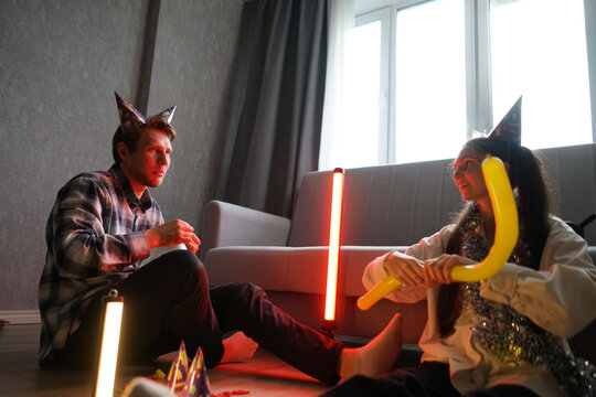 Couple enjoys a festive celebration on the floor, wearing party hats and surrounded by colorful decorations and balloons in a cozy indoor ambiance - Powered by Adobe