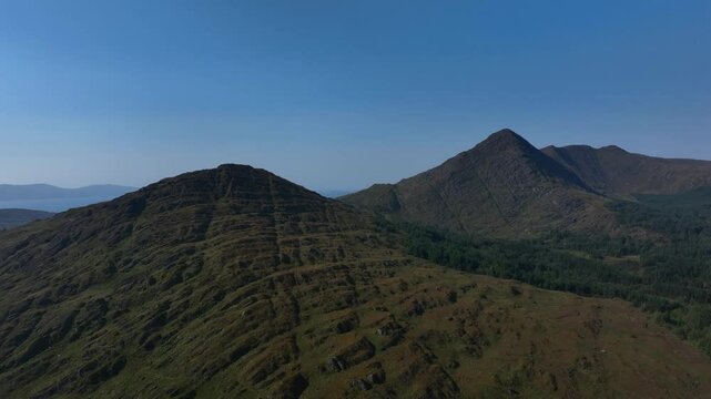 Sugarloaf, Caha Mountains, County Cork, Ireland, September 2024. Drone pushes forward and rises behind the majestic peaks surrounded the wild rugged landscape revealing the North Atlantic Ocean.