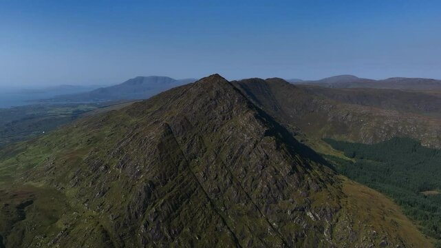 Sugarloaf, Caha Mountains, County Cork, Ireland, September 2024. Drone pushes towards the majestic summit surrounded by a wild rugged landscape under a clear blue sky by the North Atlantic Ocean.
