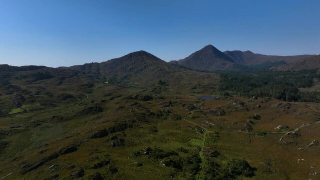 Sugarloaf, Caha Mountains, County Cork, Ireland, September 2024. Drone pulls backwards showcasing the wild rugged mountainous landscape under a clear blue sky.