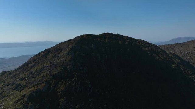 Sugarloaf, Caha Mountains, County Cork, Ireland, September 2024. Drone pulls backwards from the summit of the majestic peak under a clear blue sky with a breathtaking views of surrounding landscape.