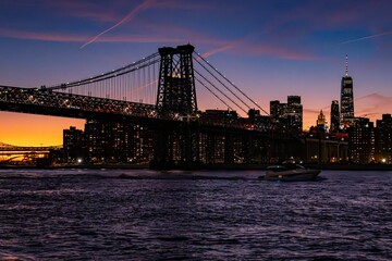 Sunset view of the Williamsburg Bridge and New York City skyline with a boat on the East River.