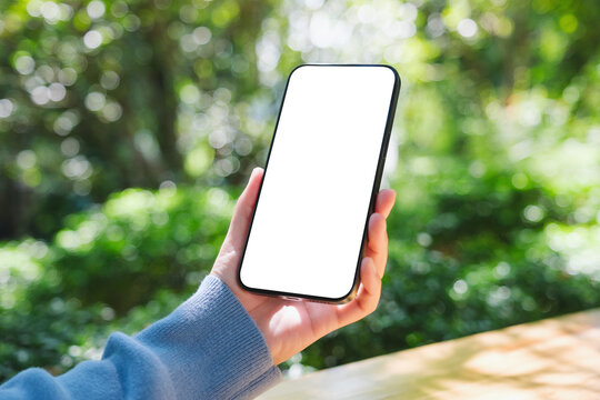 Mockup image of a woman holding mobile phone with blank white desktop screen in the outdoors - Powered by Adobe