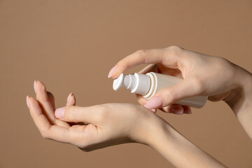 Female hand holds a bottle with dispenser with cosmetic serum. Natural cosmetic product for skin purity and hydration. Unmarked bottle with product for face skincare on beige background close-up