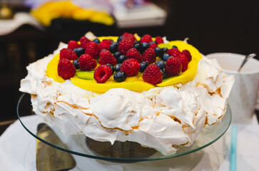 Pavlova topped with fresh fruits and mango cream. Dessert presentation, joyful mood, close-up shot, tabletop view, indoor setting, focus on vibrant colors, culinary art and celebration concept.