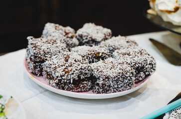 Australian lamingtons coated with chocolate and coconut. Dessert display, inviting mood, close-up angle, arranged on a plate, indoor setting, focus on texture, sweet treat and culinary concept.