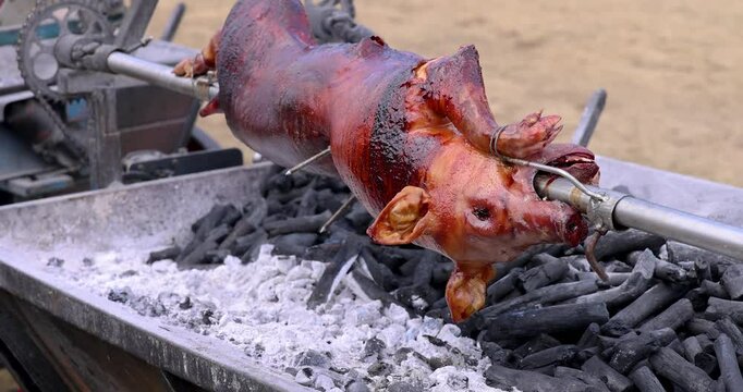 Roasted whole pig on fire. Grilled pig on skewer. Roasting pig on a spit turns slowly roasting it. Barbecue. Street food. 4k. Lechon or Suckling Pig a popular dish in Spain, Philippines and Italy