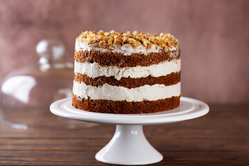 Homemade pumpkin cake with coconut cream on a stand on wooden background. Vegan dessert, sugar, gluten and lactose free.