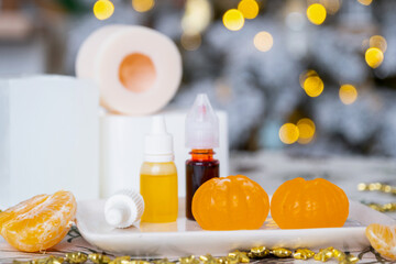 Handmade soap in the form of Orange tangerine  with bottles of dye, flavor, a block of glycerin soap base, silicone mold, on background of Christmas tree with golden light. Soap as gift new year