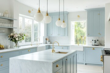 A bright kitchen with light blue cabinetry, brass hardware, and soft pendant lighting, centered around a large marble island with an integrated sink and minimalist decor.