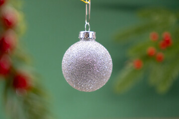 silver glitter christmas ornament hanging, holiday bauble with green and red background decor