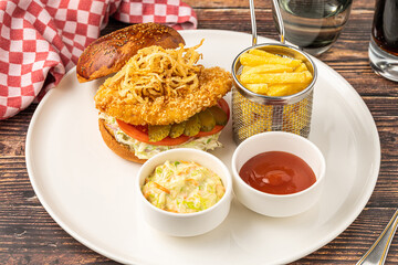 Chicken burger served with fries and sauces on a white porcelain plate