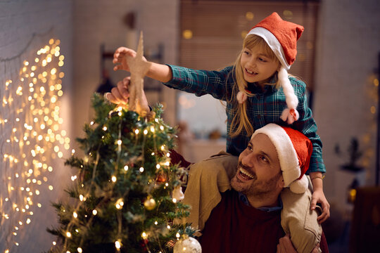 Happy father and daughter decorating Christmas tree and putting star on top of it.