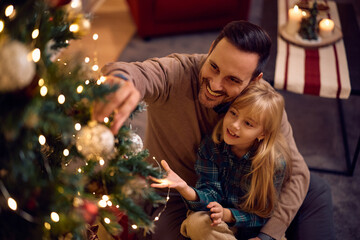 Happy man decorating Christmas tree with his daughter at home.